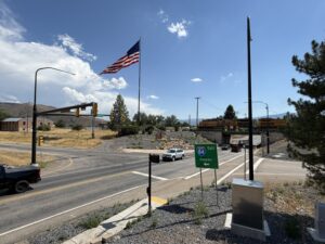 Traffic signal at the intersection of SR-66 (300 North) and I-84 Eastbound Ramps in Morgan, Utah, with vehicles stopped at the light, an overpass with a train visible in the background, and mountains in the distance.