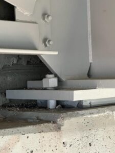Close-up of a newly painted light-gray bridge bearing assembly with anchor bolt, nuts, and rubber pad on a concrete pier